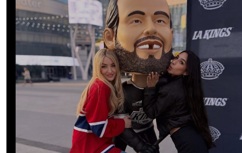 Two cast members posing with a giant LA Kings bobblehead outside the arena